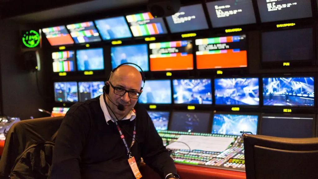 Paolo Monesi in regia mobile televisiva davanti a una parete di monitor